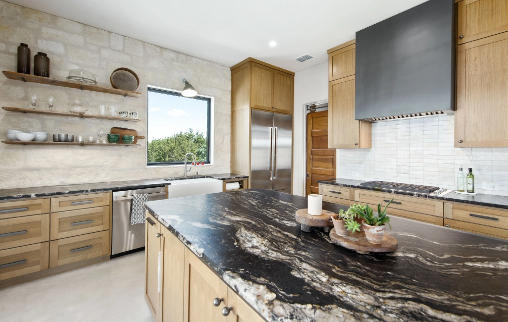 Modern kitchen featuring wooden cabinets, marble countertops, open shelving, a large island with a sink, and stainless steel appliances. A window provides natural light.