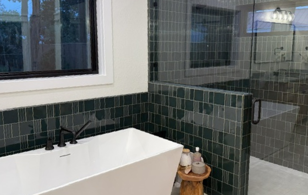 A bathroom remodel features a large freestanding tub and walk in shower with dark blueish green tiles and matte black fixtures.