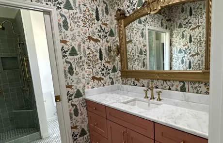 A bathroom features a marble countertop with a sink, gold fixtures, and a large ornate mirror above. The walls are covered with nature-themed wallpaper, and a shower is visible to the left.