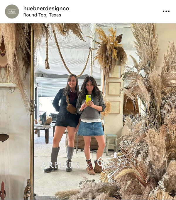 Two women stand together in a decorated space with dried floral arrangements.