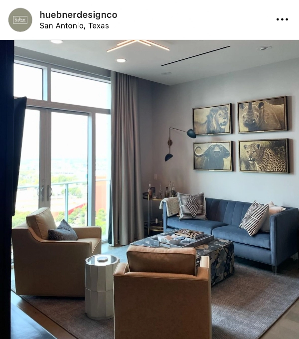 A modern living room with two beige chairs, a blue sofa, a patterned ottoman, and four framed wildlife pictures above the sofa. A floor-to-ceiling window opens to a view outside.